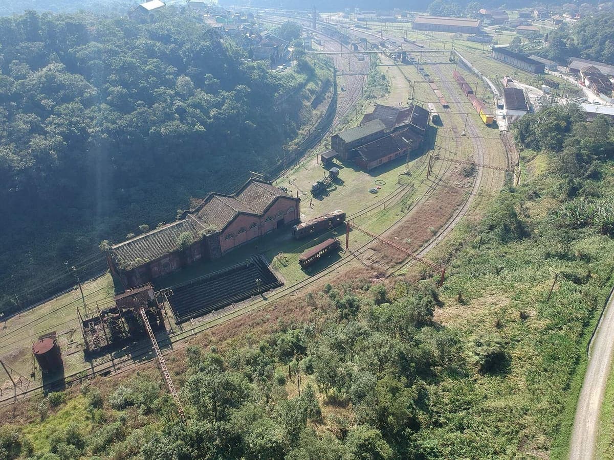 Vista aérea dos galpões de tijolo do antigo sistema funicular em Paranapiacaba, hoje museu, cercados de Mata Atlântica e pátios ferroviários
