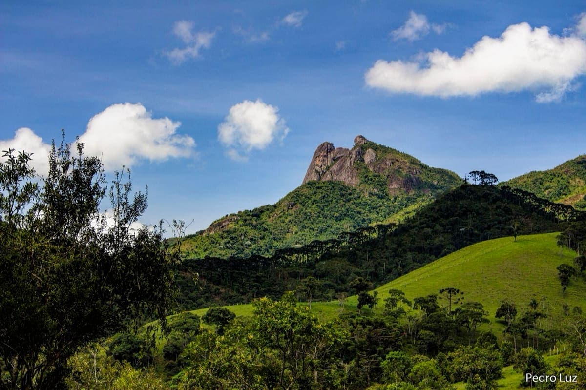 Pico da Pedra Selada, com os dois blocos de rocha em forma de sela, acima de pastos e mata em Visconde de Mauá