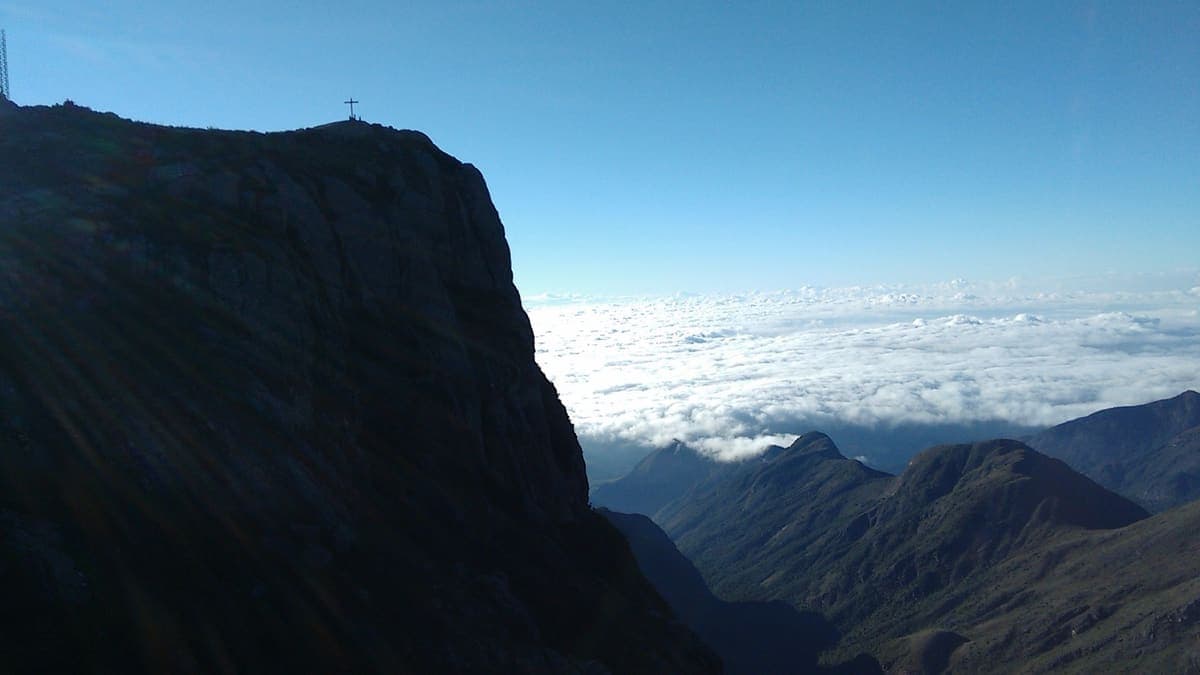 Pico da Bandeira visto do Pico do Calçado, com o cruzeiro no topo e um mar de nuvens sobre os vales do Caparaó